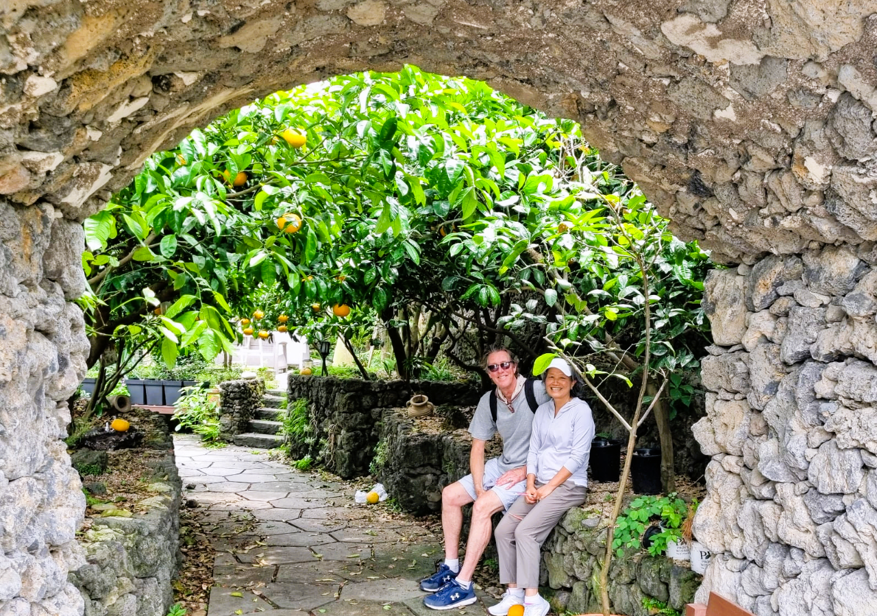 Canadian couple Linda and Hakan sitting by traditional stone walls on Jeju Island South Korea with mandarin trees in background