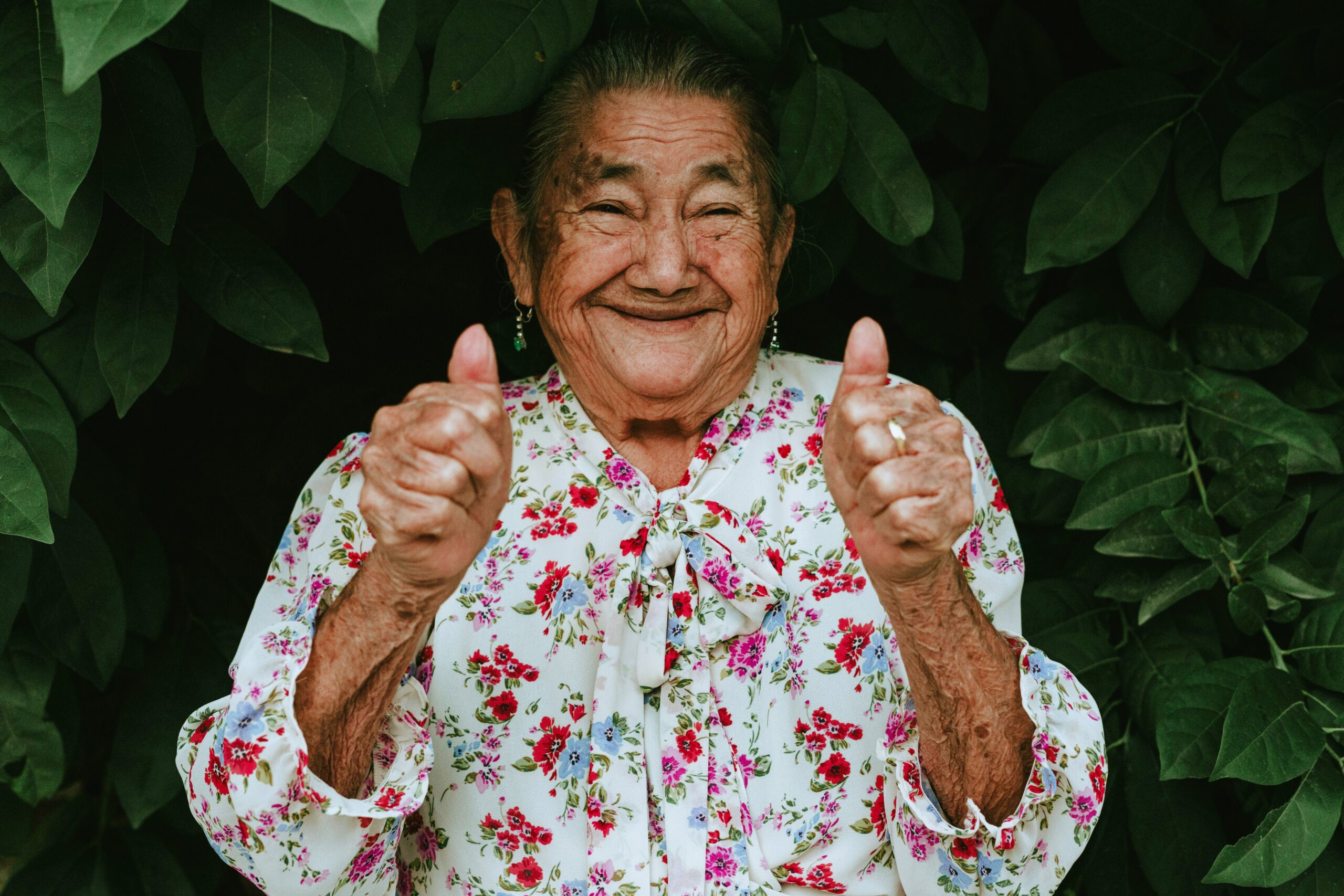 An elderly woman smiling warmly and giving a thumbs up, reflecting the warmth of a greeting returned with enthusiasm.
