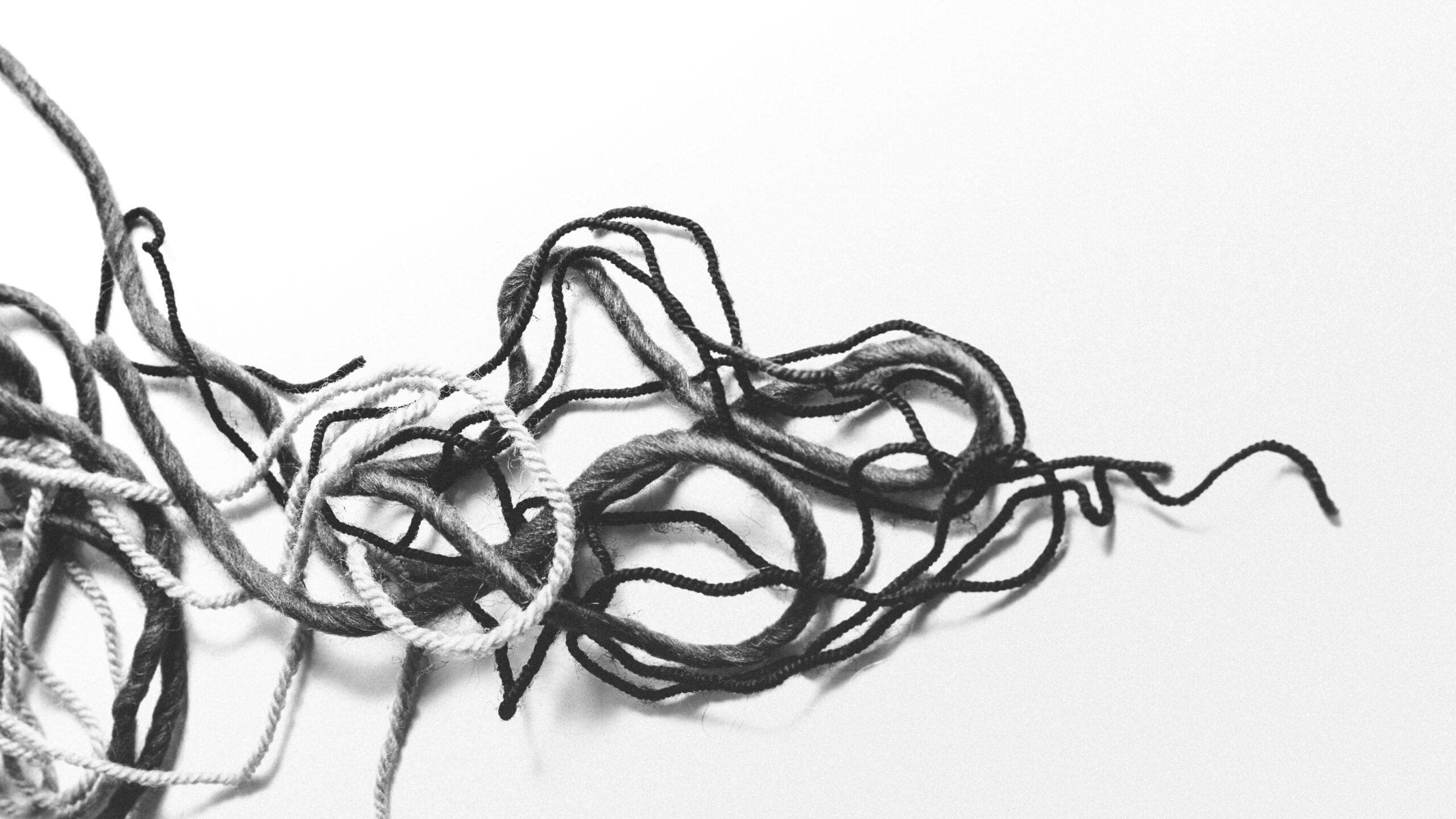 Black and white close-up of tangled yarn, most strands knotted together with a few loose threads trailing off to the side.